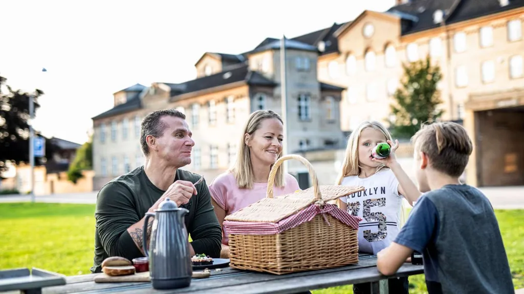 A family eats lunch at a bench in the Prison Park at FÆNGSLET in Horsens