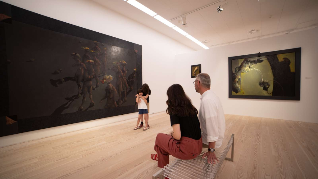 Et par sidder på en bænk og kigger på et maleri af Michael Kvium hos Horsens Kunstmuseum