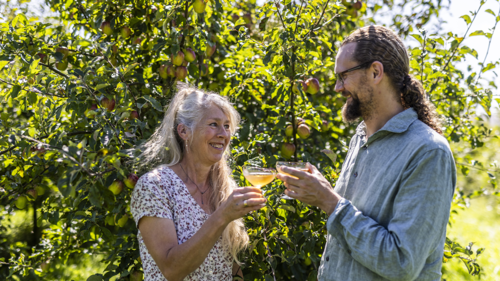 Lone Landmand and Søren Sørøver toast with cider in front of apple trees