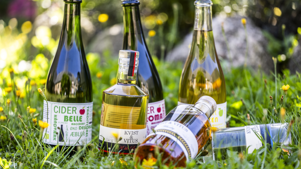 Flaschen mit gemischtem Wein und Cidre von Brandbygegaard liegen auf dem Rasen