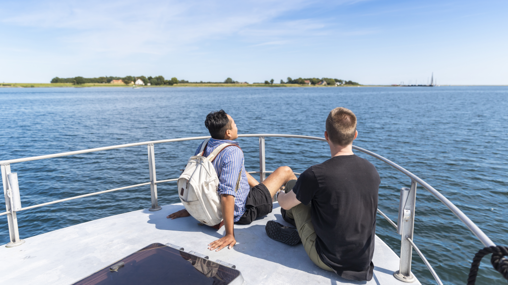 Two men are sitting on the bow of the bicycle ferry Alrø-Hjarnø as it sails towards Hjarnø