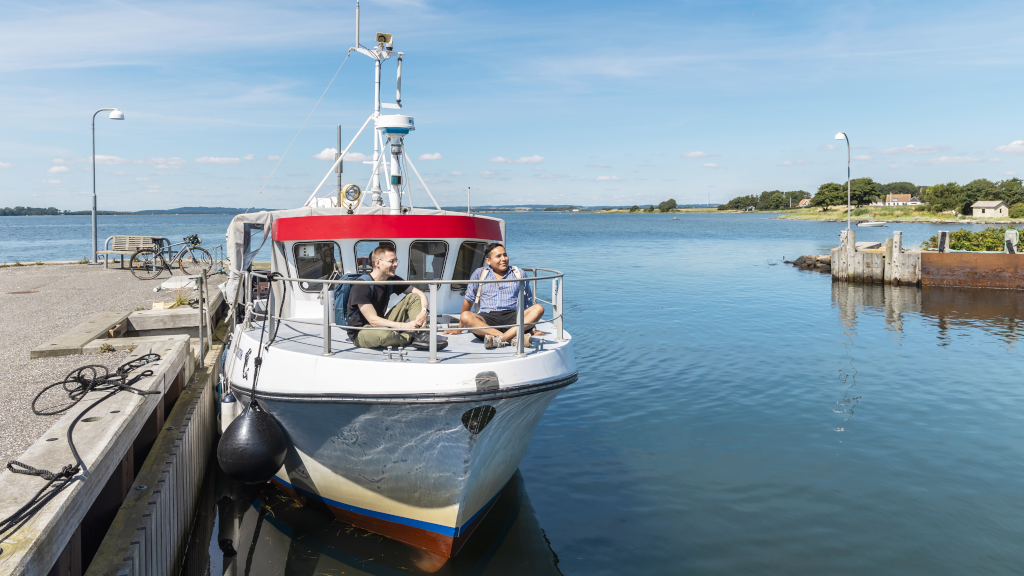 Two men are sitting on the bicycle ferry Alrø-Hjarnø while it is moored at the quay at Hjarnø