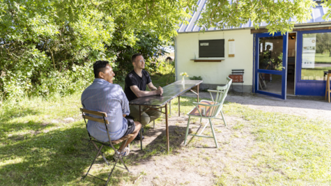 To mænd sidder ved et havebord på græsplæne foran Det Grafiske Magasin