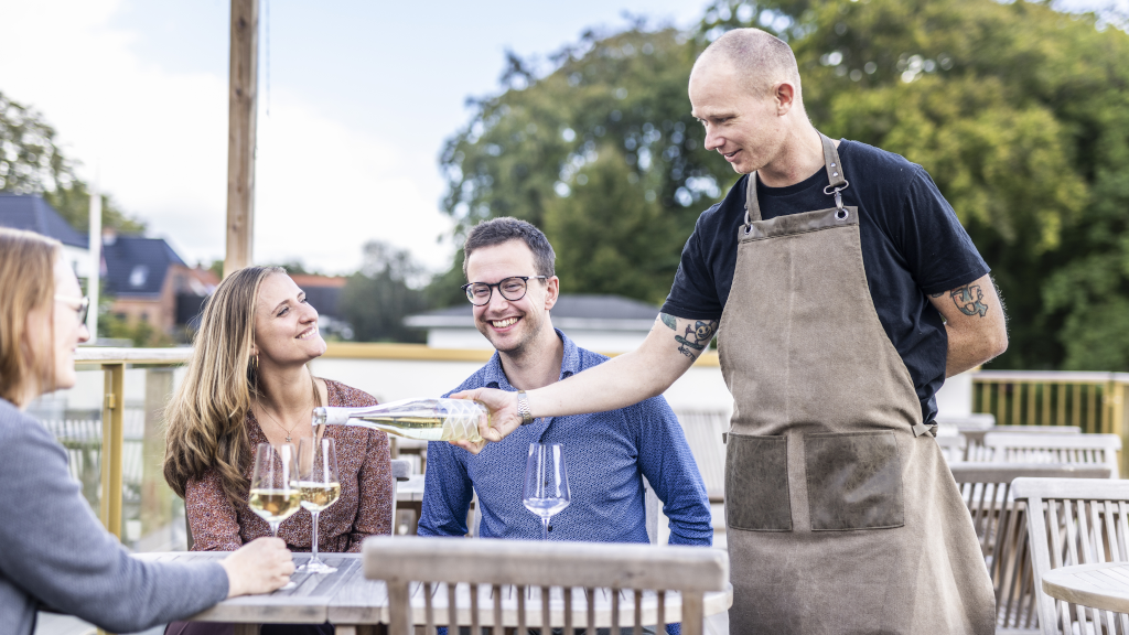 Waiter pours white wine into glass at the terrace of Water of Life in Brædstrup