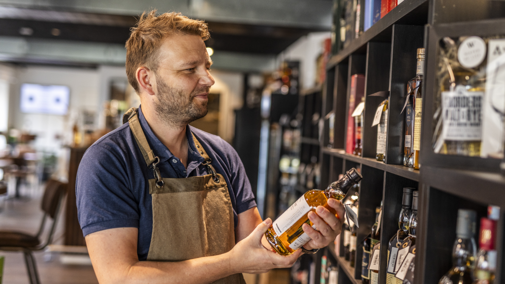 The owner Theis from Water of Life stands in his store holding a bottle of whisky