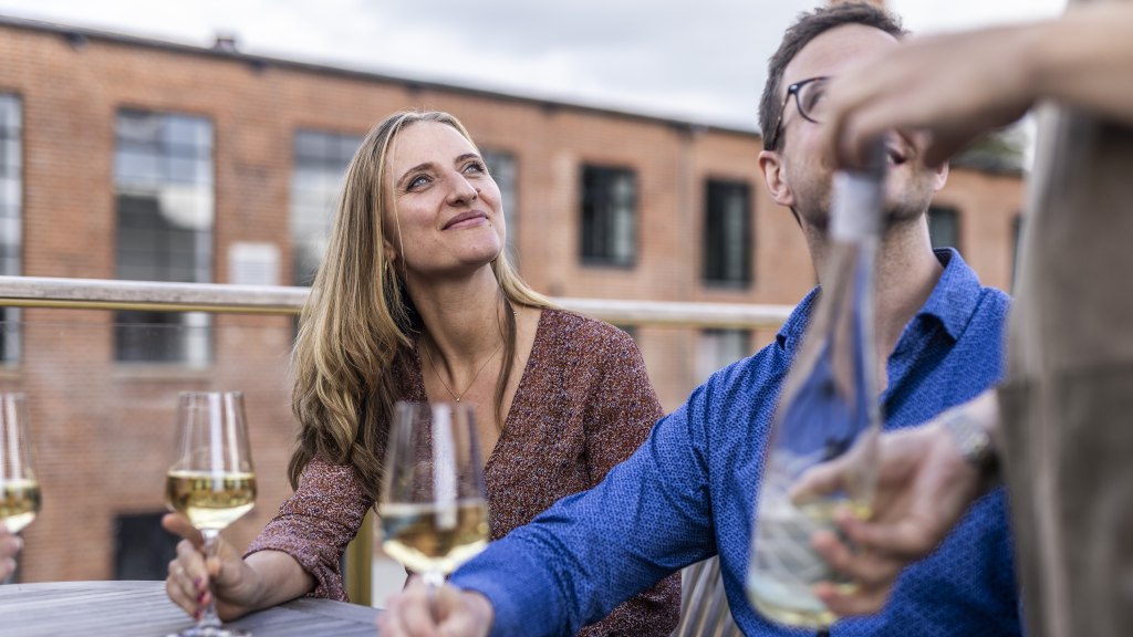 A man and a woman are being served white wine by a waiter on the terrace at Water of Life