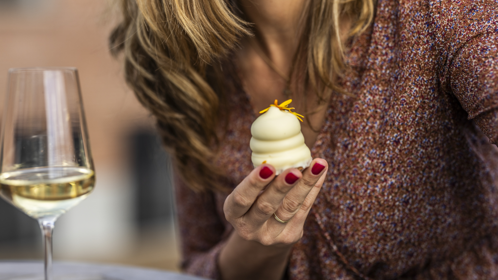 A woman is eating a chocolate-covered marshmallow treat and drinking white wine from Water of Life in Brædstrup