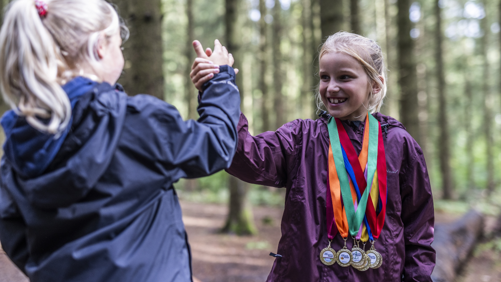 Two girls are giving each other a high-five in Ring Forest, holding the medals they earned from all the treasure hunts in Destination Kystlandet