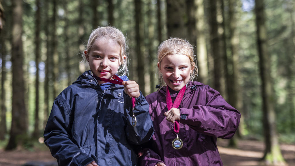 Two girls are standing in the woods, holding their medals from the Brædstrup Treasure Hunt