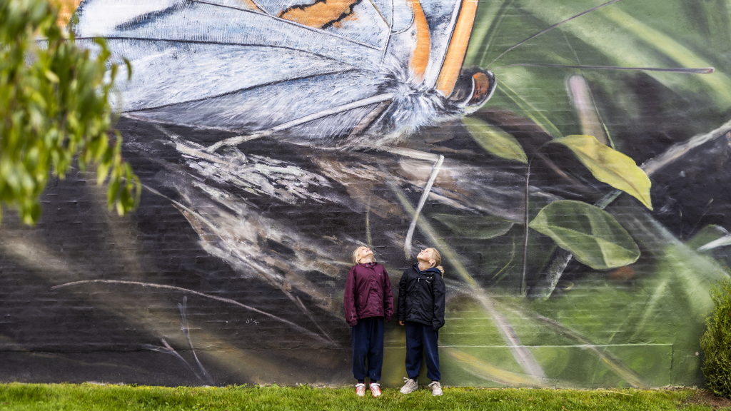Two girls are standing in front of a butterfly mural in Brædstrup