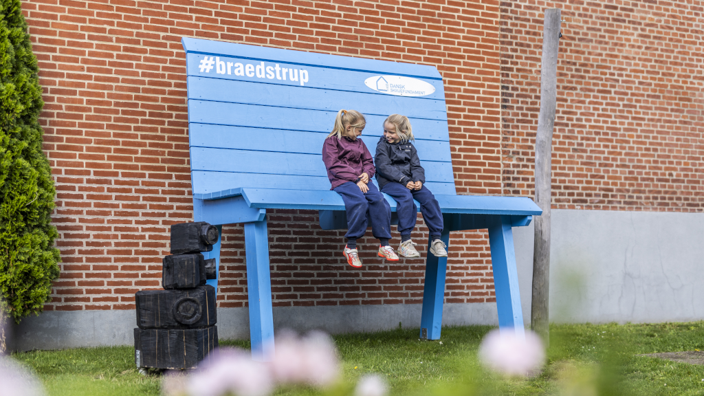 Two girls are sitting on a very high bench in Byhaven in Brædstrup