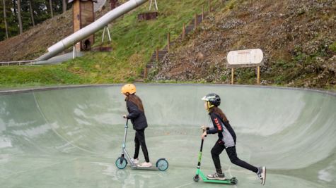 To børn kører på løbehjul i skatearenaen i Juelsminde Naturlegepark