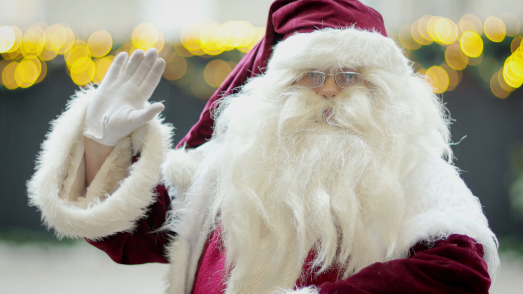 Santa Claus is waving in front of Christmas lights
