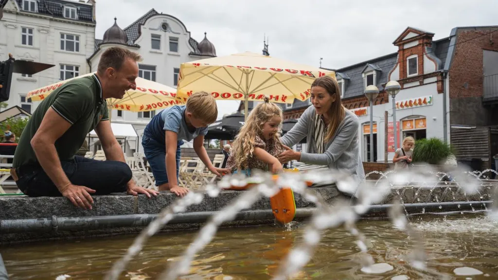 En familie sidder på kanten af springvandet på Torvet i Odder