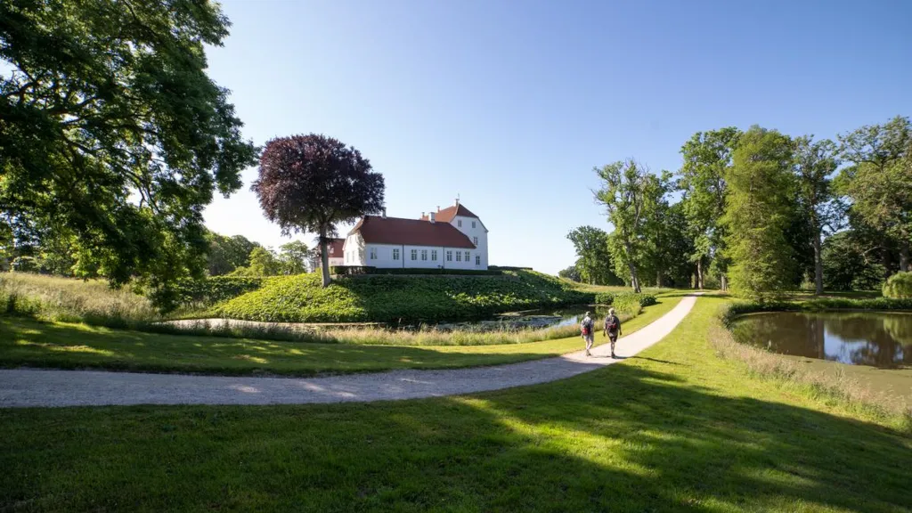 Two men are walking on a path through Palsgaard Castle Park with Palsgaard Castle in the background