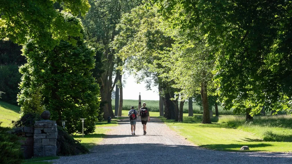 Two men are walking down an avenue towards a monument in Palsgaard Castle Park