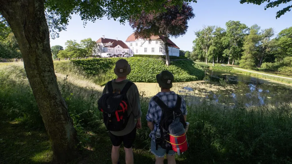 Two men are standing by the moat in Palsgaard Castle Park and looking at Palsgaard Castle
