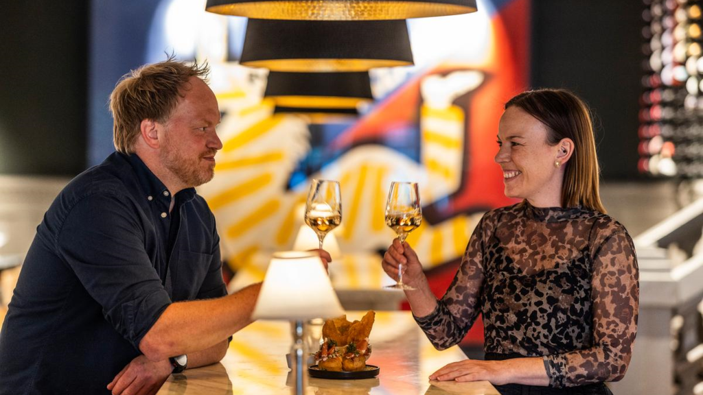 A couple sits in the wine bar at Jørgensens Hotel and toasts with white wine