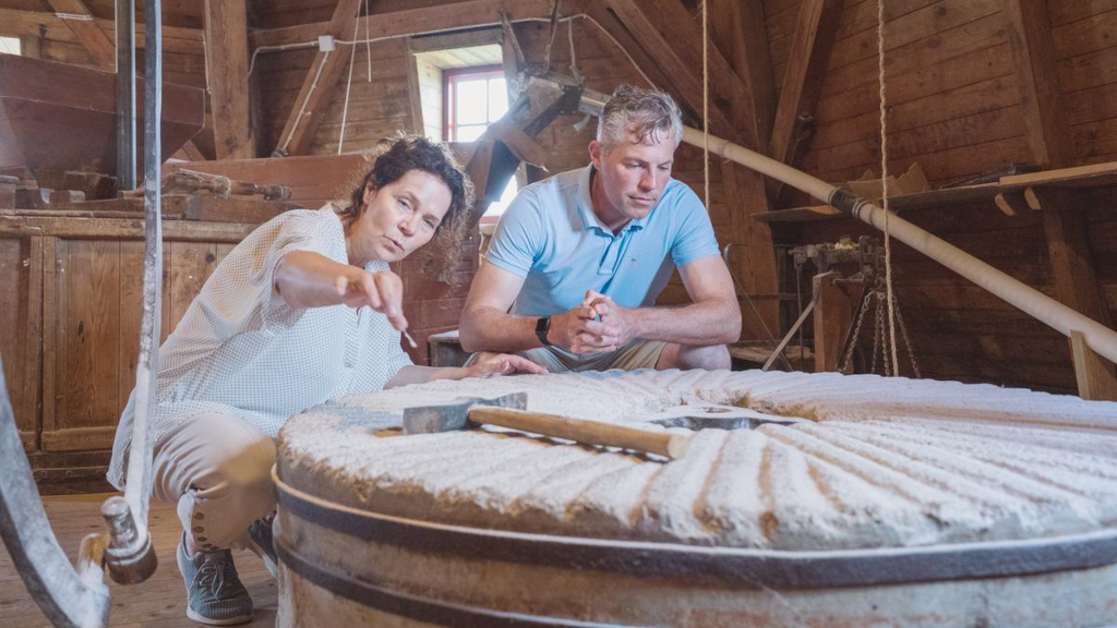 A couple is studying a mill wheel in the exhibition at Uldum Mill Museum
