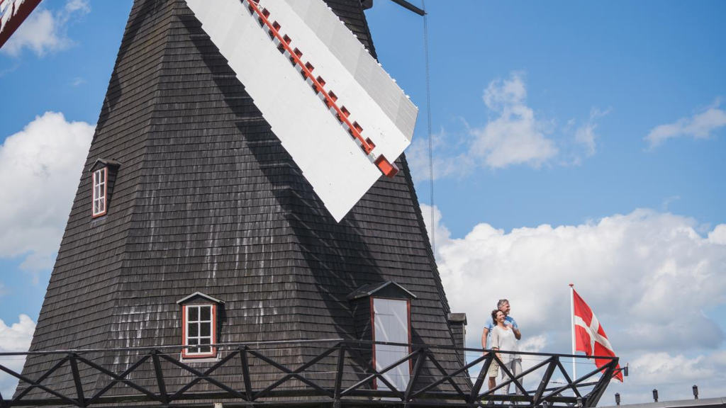 A couple stands on the balcony of Uldum Mill next to a Danish flag