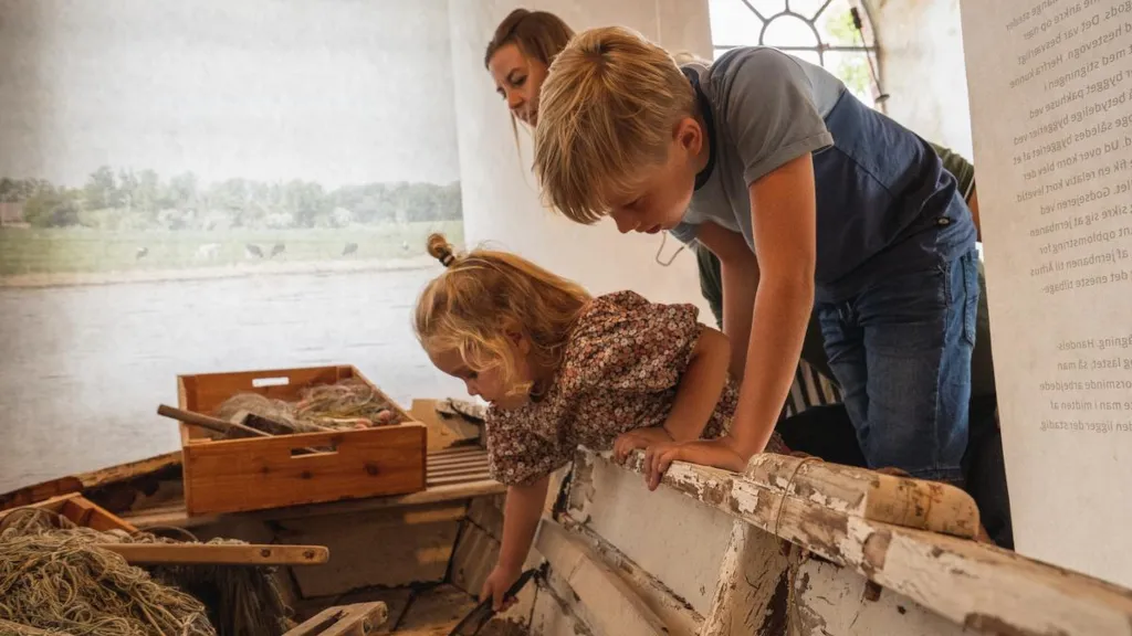 En familie kigger ned i en båd i en udstilling på Odder Museum