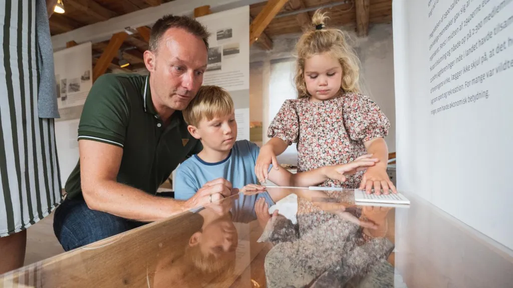 Far og to børn kigger ned i glasmontre i udstilling på Odder Museum