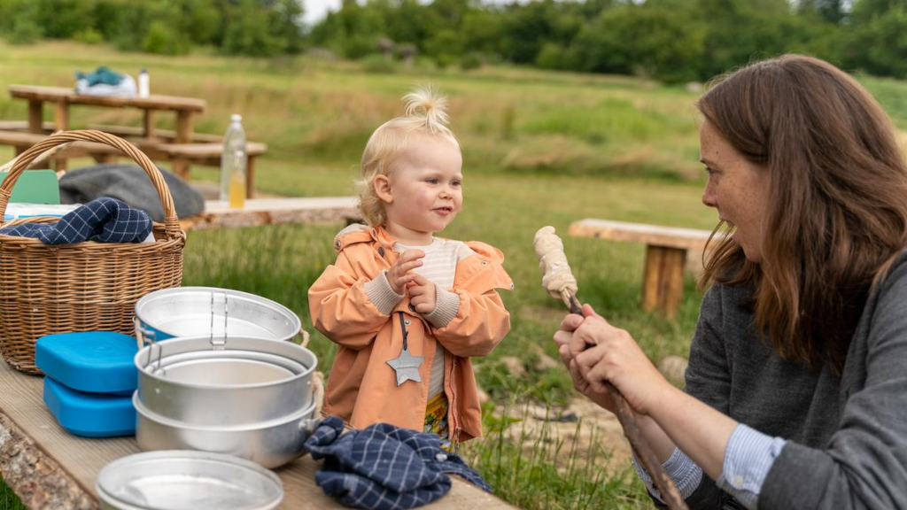 A mother is holding out a twisted bread towards a little girl at the shelter site in Eventyrskoven