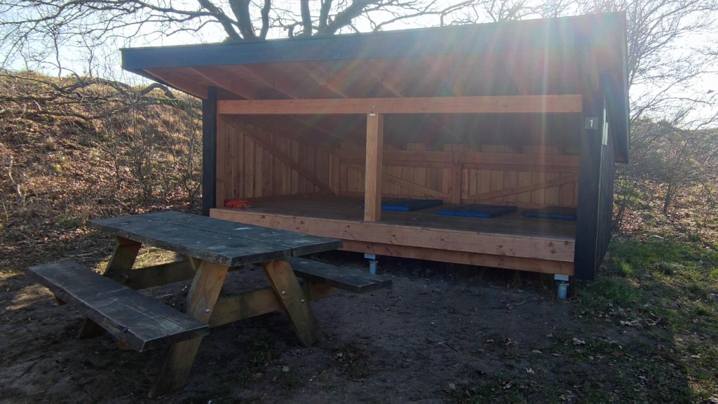 A table/bench set is standing in front of a shelter at the shelter site in Lundum