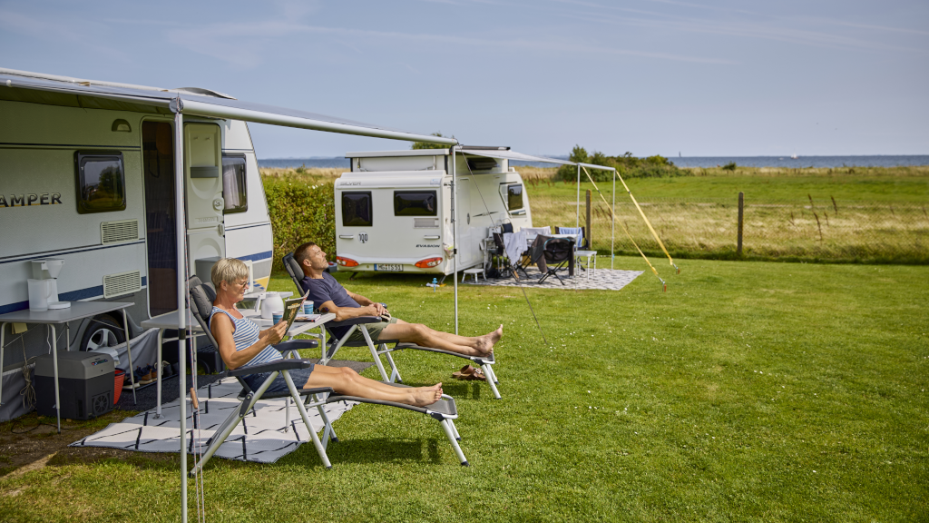 A couple is sitting in camping chairs, sunbathing at Hygge Strand Camping
