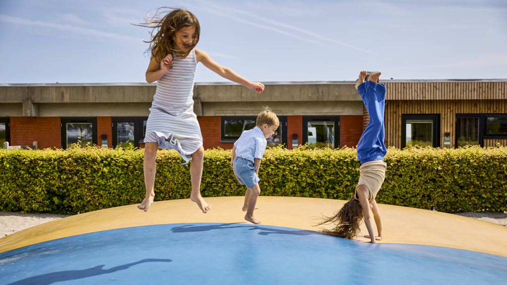 Children are jumping on the jumping pillow at the playground at Hygge Strand Camping