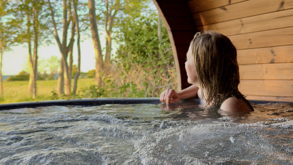 Woman sitting in a wilderness hot tub at Campingpladsen Endelave, looking out at the nature