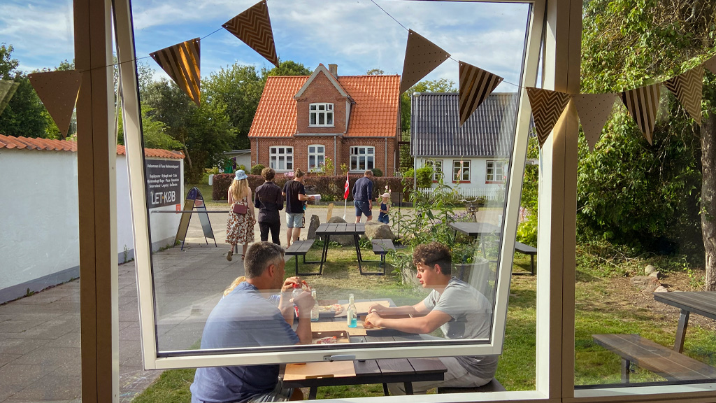 Gæster sidder ved borde/bænkesæt udendørs ved caféen hos Tunø Købmandsgård