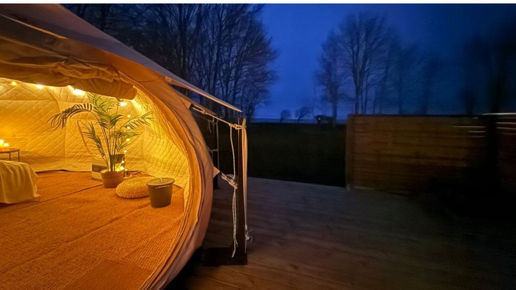 Glampingtelt set udefra om aftenen med kig ind