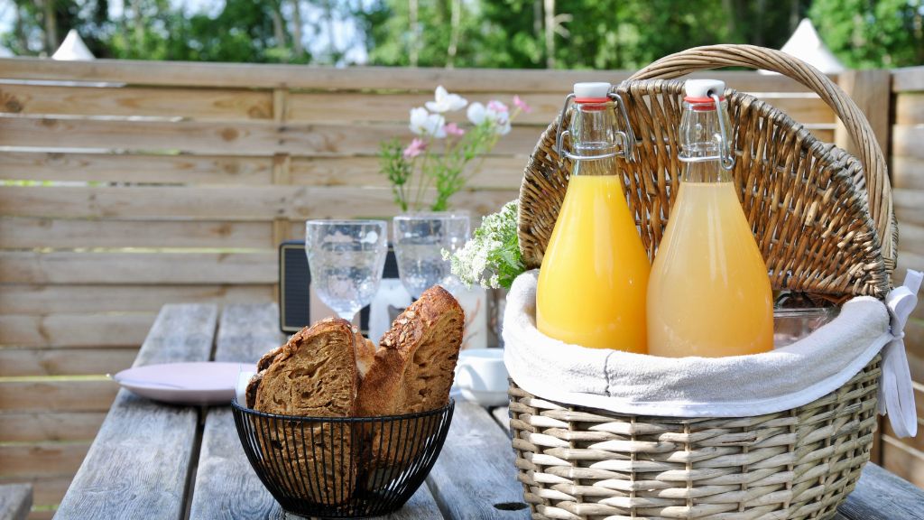 A basket with bottles of morning juice and a small basket of bread on a table at Endelave Campsite.