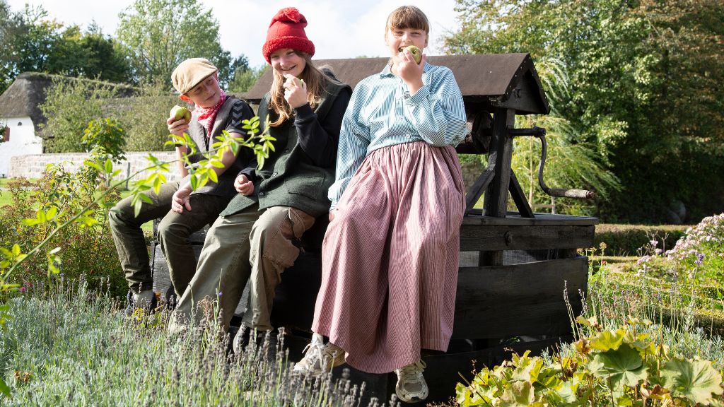 Three children at Glud Museum eating apples and dressed in traditional period costume.