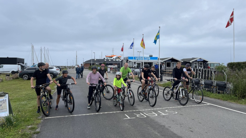Børn og voksne står med deres cykler ved startstregen til et cykelløb på Endelave Havn