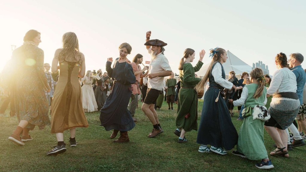 Mennesker i middelalderdragter danser på græs til Horsens Middelalderfestival