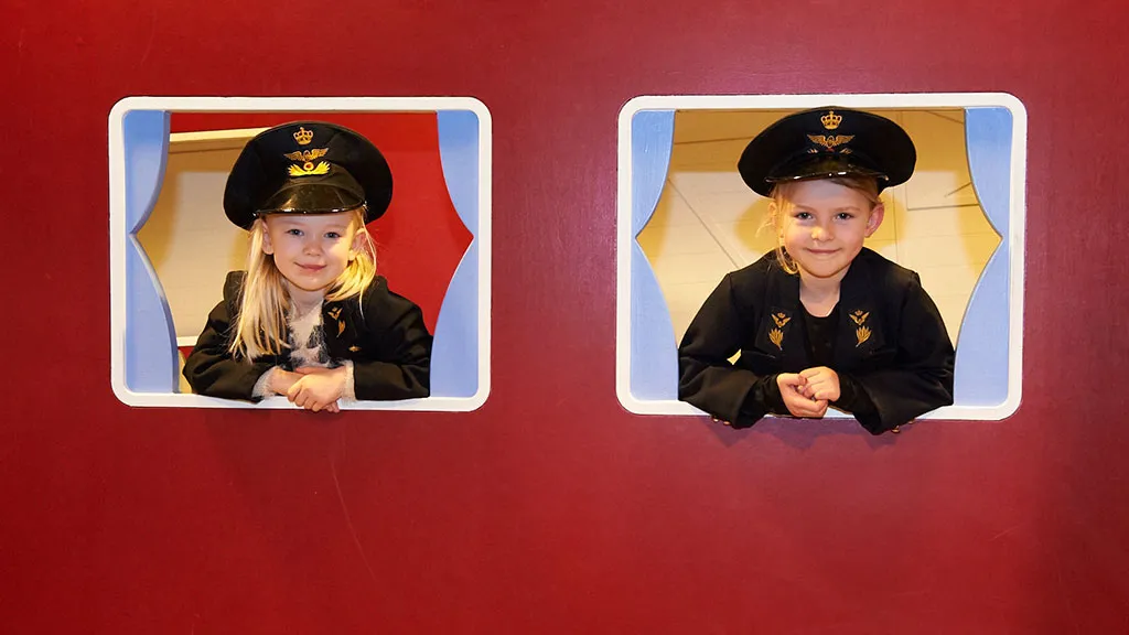 Two girls in uniforms playing at the children's train station.