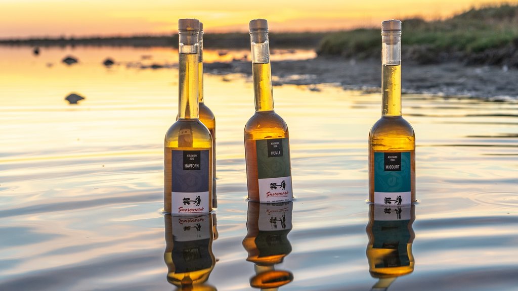 Drei Flaschen Apfelmet von Snoremark stehen bei Sonnenuntergang im flachen Wasser.