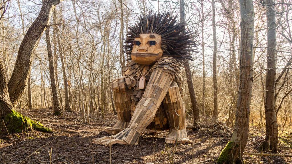 A large wooden troll with spiky branch hair crouches in a bright forest