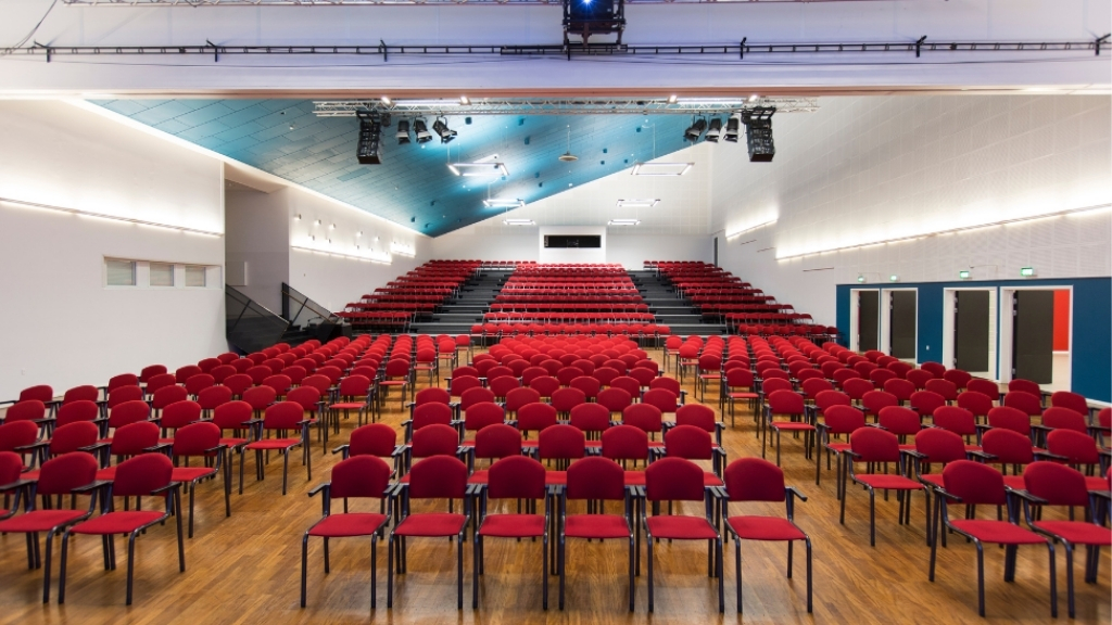 Conference hall at Roskilde Kongrescenter with red chairs and elevated seating area.