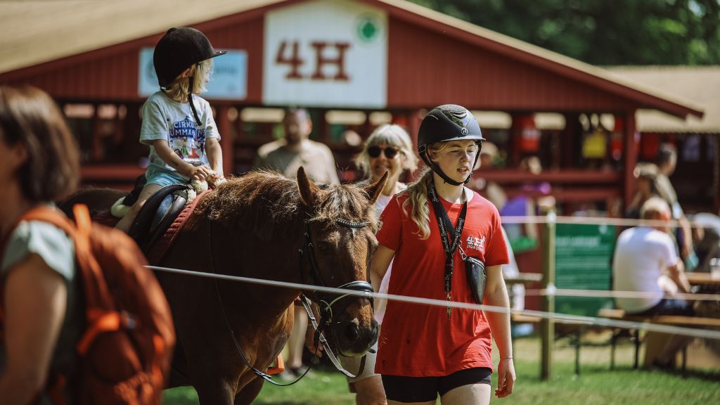 Barn rider på hest ledsaget af ung hjælper ved Roskilde Dyrskue