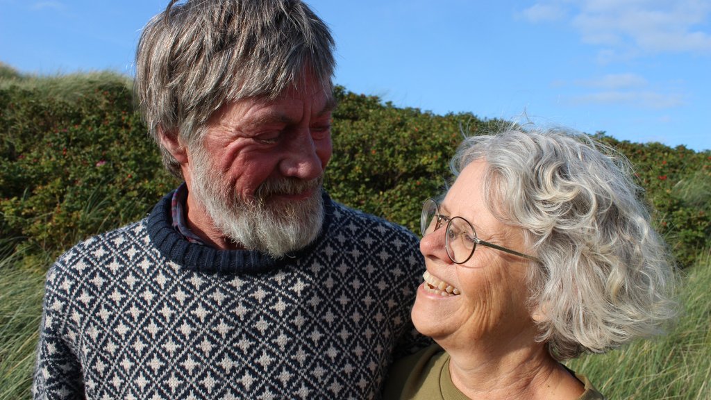Host couple from Højtoft B&B smiling at each other in green surroundings.