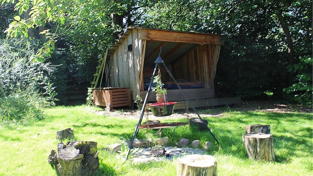 Shelter with campfire site and seating in green surroundings at Højtoft B&B.