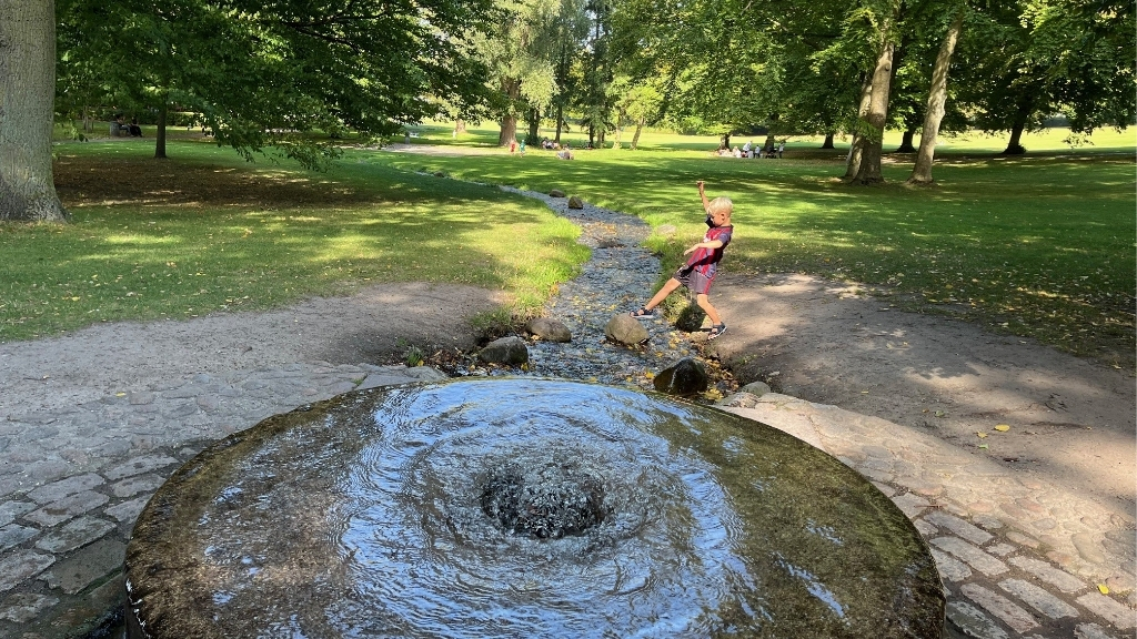 Spring source in Roskilde Bypark with boy playing at the water’s edge.