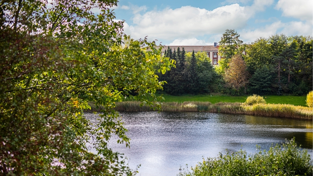 Udsigt til Scandic Roskilde Park fra sø omgivet af træer og grønt.