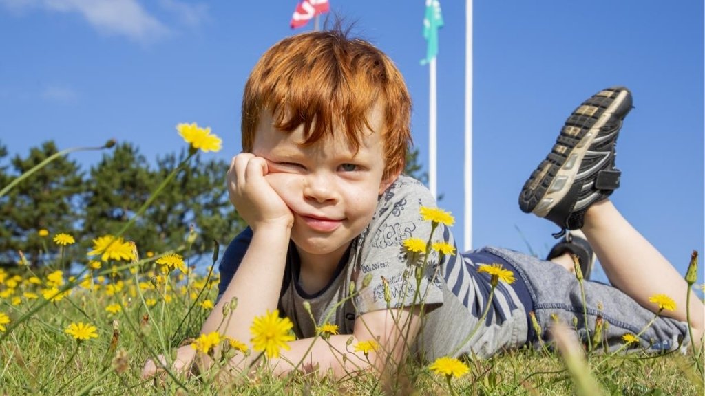 Child playing in the grass at Kulhuse Camping with flags in the background.