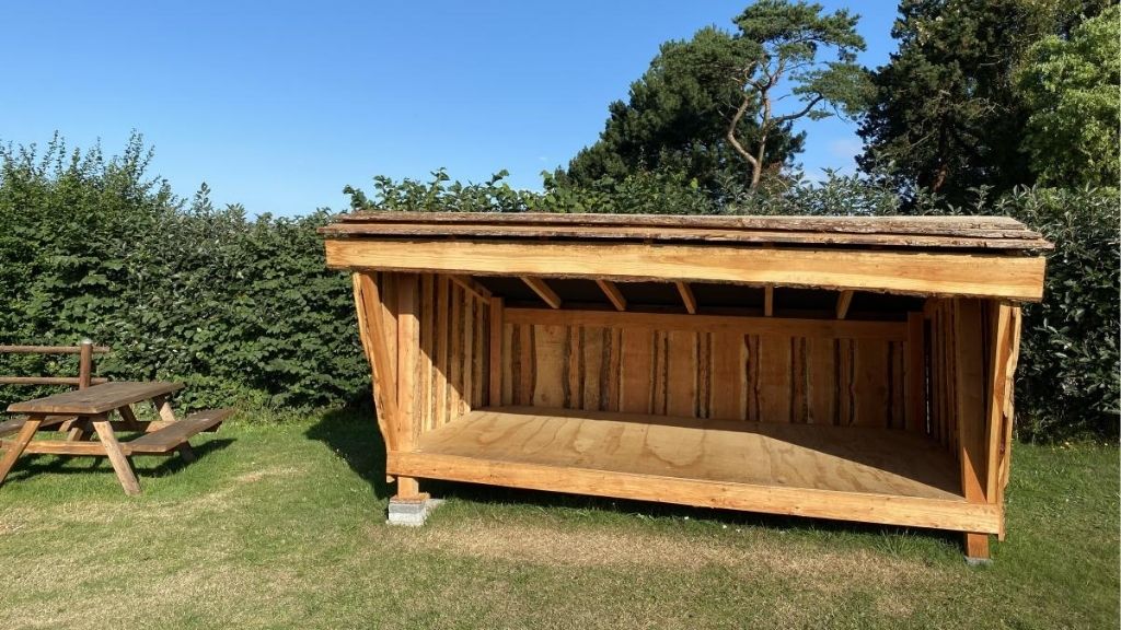 Shelter and picnic table at Kulhuse Camping surrounded by hedges.