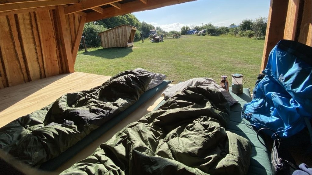 View from a shelter at Kulhuse Camping with sleeping bags and grassy area in front.
