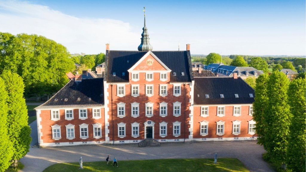 Aerial view of Jægerspris Castle with red facade and surrounding green park area.